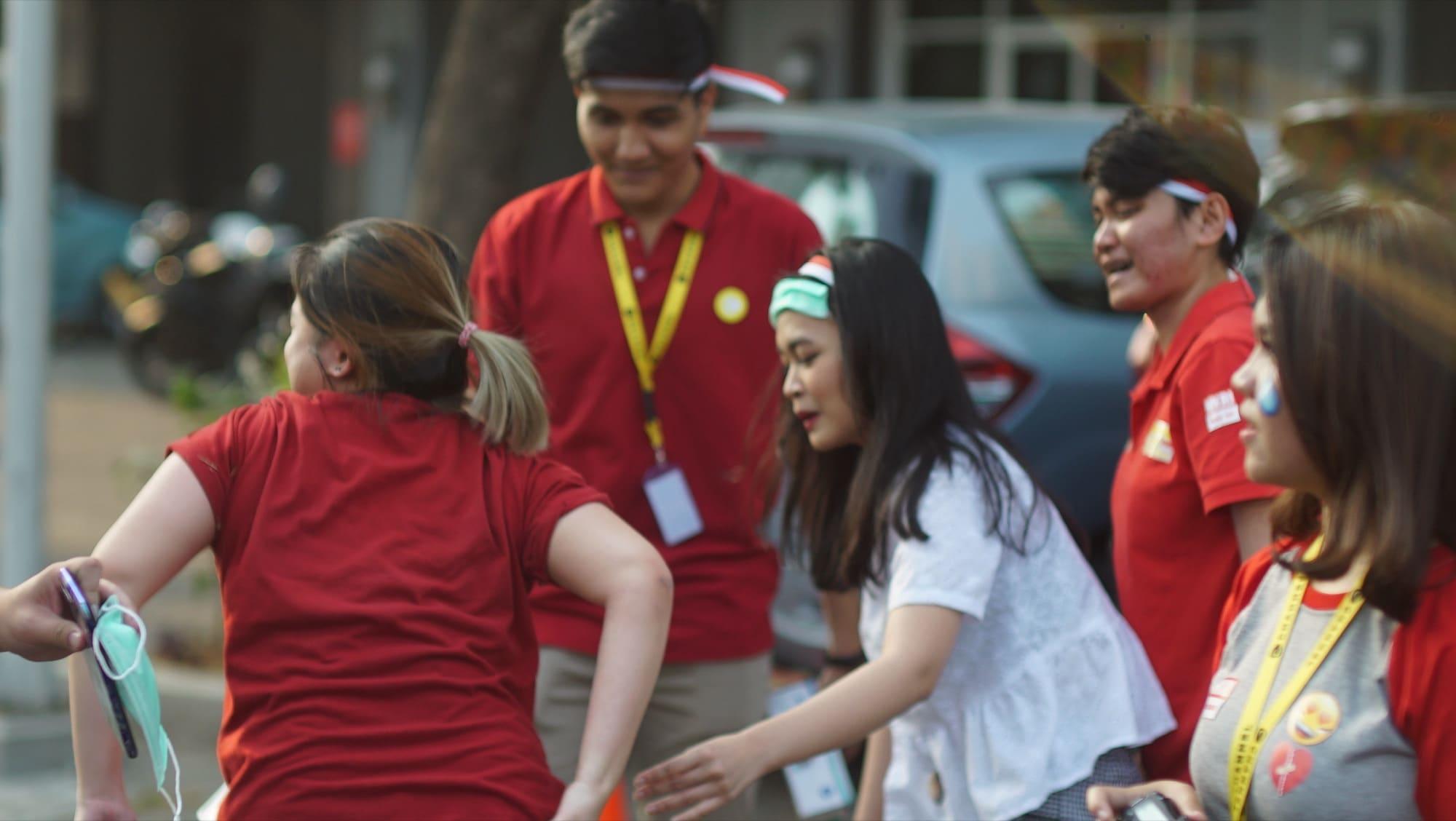 Colleagues in red polo shirts and Indonesian flag headbands mid-game outdoors on Independence Day.