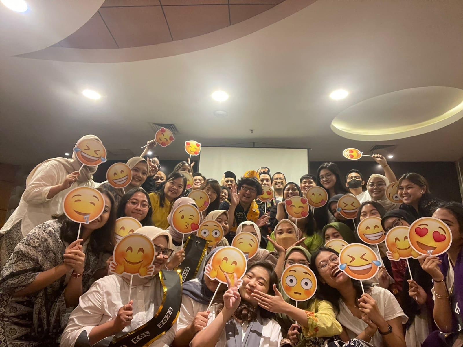 The team crowded together at an evening party, everyone holding a printed emoji face on a stick.