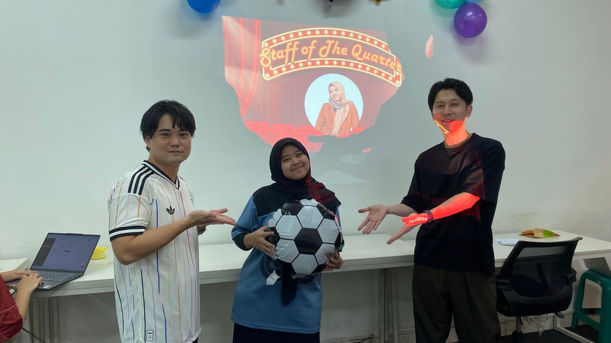 A Staff of the Quarter presentation: three colleagues either side of a football balloon, the award slide projected on the wall behind.