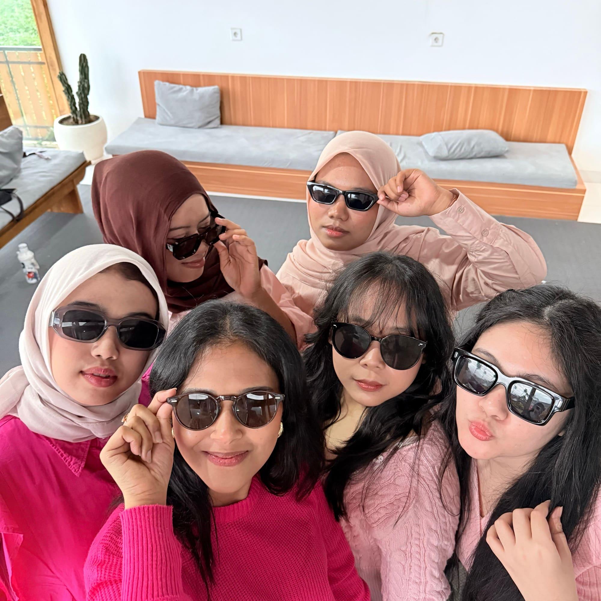Six colleagues lean into the camera in sunglasses in a villa common room during a team trip.